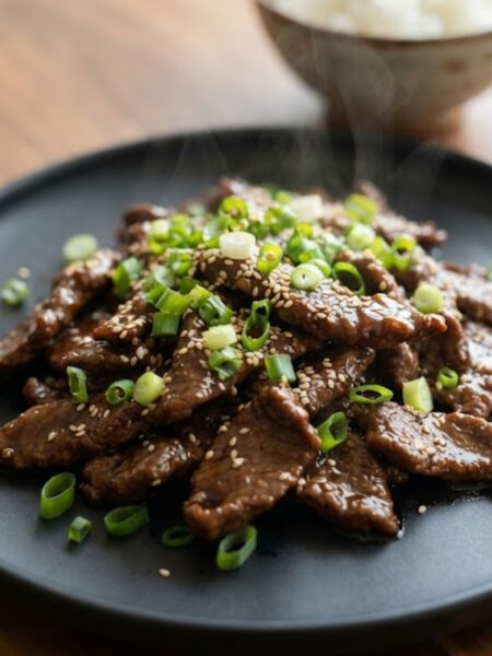 Tender Mongolian Beef stir-fried in a rich garlic soy sauce with green onions, beautifully served on a white ceramic plate.