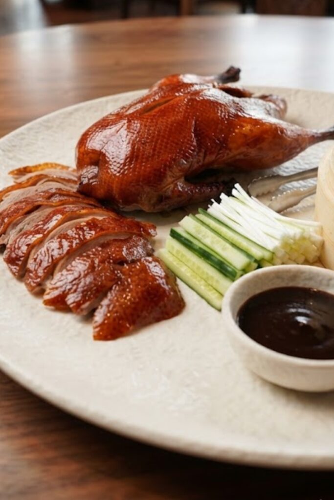 Authentic Chinese Peking Duck with crispy golden skin, tender sliced meat, Mandarin pancakes, cucumber, green onions, and hoisin sauce.